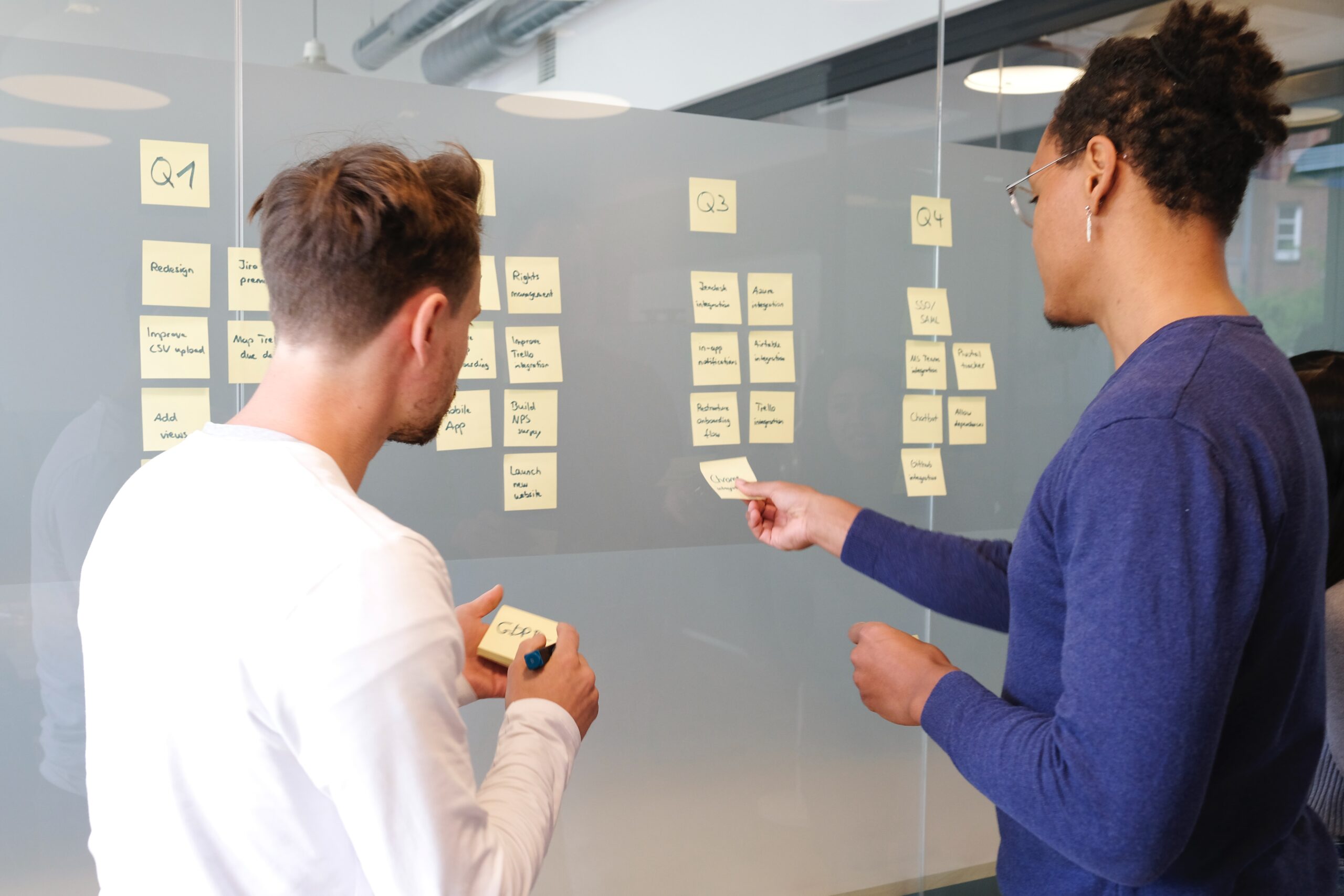 airfocus-v89zhr0iBFY-unsplash two people standing in front of a board with post it notes sharing thoughts to reflect a collaborative environment for marketing teams